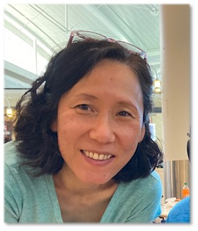 Close up photograph of blog post contributor Yuko Caras smiling into the camera with glasses on top of her head